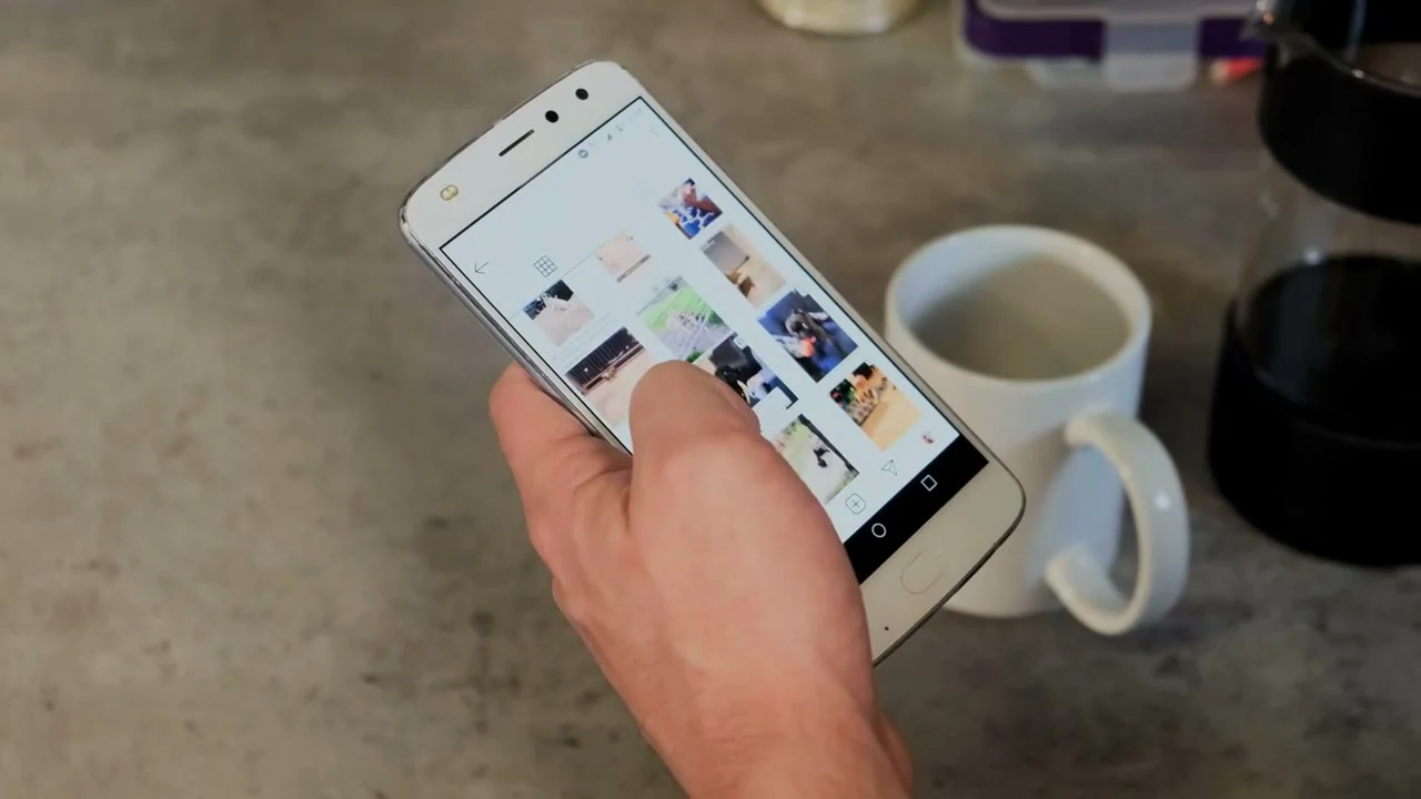 O persoană navighează pe telefon în timp ce își toarnă cafeaua.